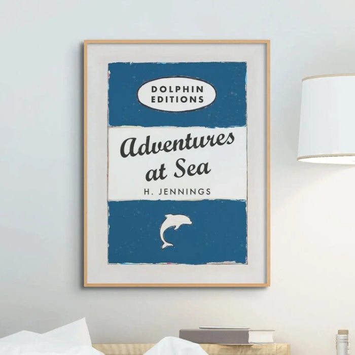 A vintage style book cover art print with the title 'Adventures at Sea' and the author H. Jennings. Framed poster with 'Dolphin Editions' design on a wall.