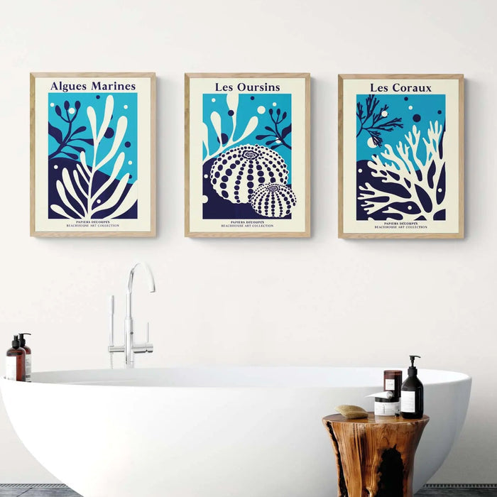 A set of three bathroom art prints featuring coral and seaweed designs in a coastal art style, displayed above a bathroom sink.