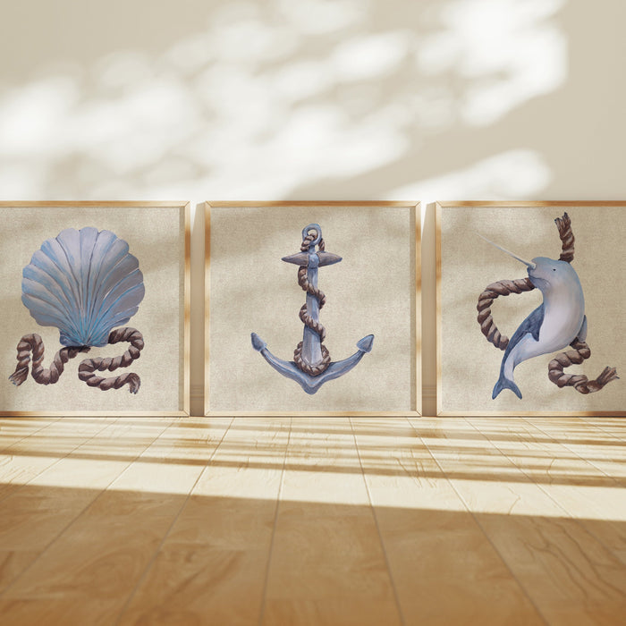 Three framed artworks of a shell, an anchor, and a whale on a wall with sunlight casting shadows.