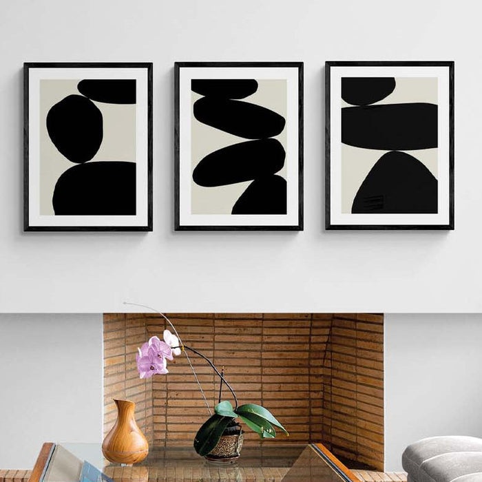 Three abstract black and white artworks on a wall above a fireplace in a living room.