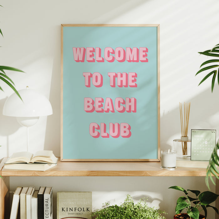 Framed typography poster with 'Welcome to the Beach Club' text on a shelf with decor items.