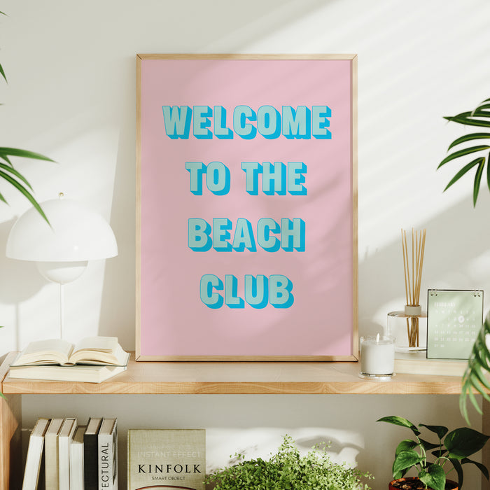 Framed poster with 'Welcome to the Beach Club' text on a pink background, displayed on a shelf.