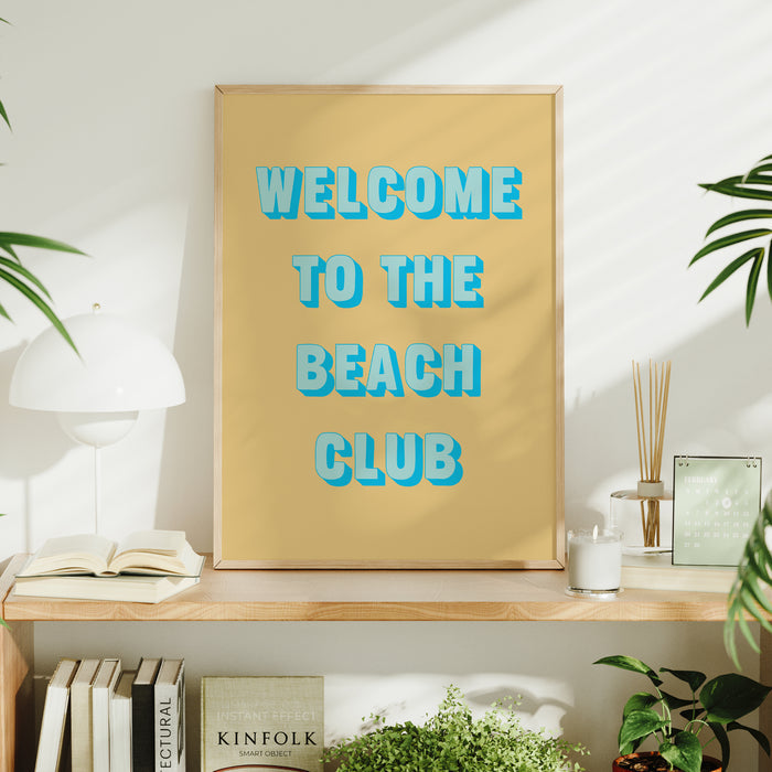 Framed artwork with 'Welcome to the Beach Club' text on a shelf with decor items.