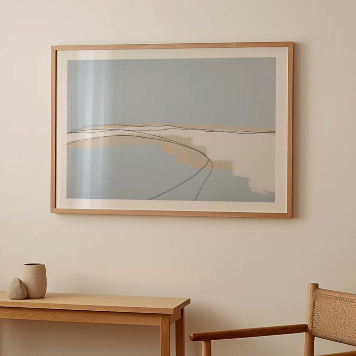 Framed abstract coastal artwork on a wall with a wooden table and chair in the foreground.