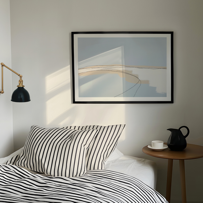 Modern bedroom with striped bedding, abstract sea painting, and a side table.