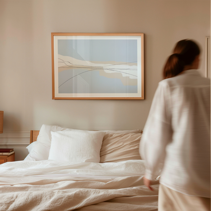 Person standing by a bed in a bedroom with abstract art on the wall