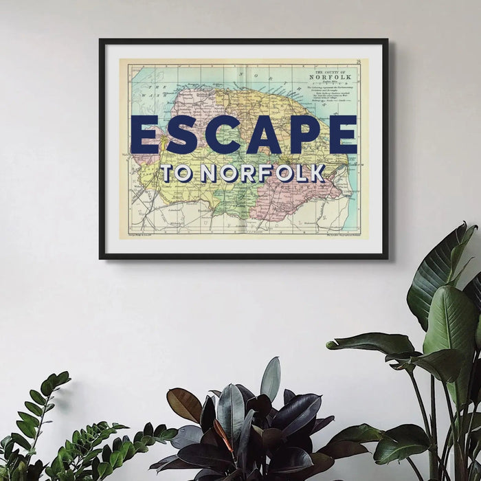 Framed Norfolk vintage map art print with the text 'ESCAPE TO NORFOLK' overlayed on a map of Norfolk. Displayed in  living room above house plants.