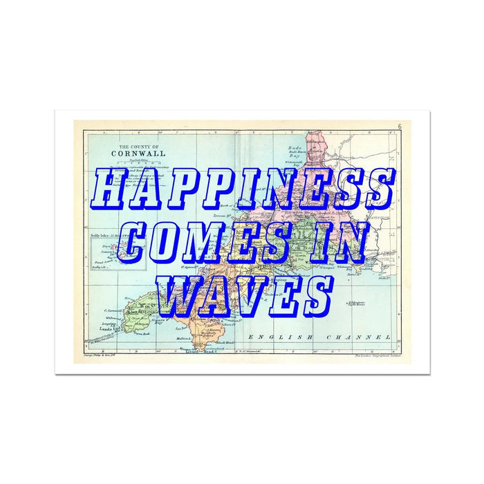 A framed art print featuring a vintage map of Cornwall with the text 'Happiness Comes In Waves' overlayed on top in a bold, blue font.