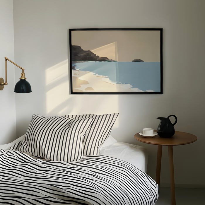 Bedroom with striped bedding, a side table with a pitcher and cup, and a framed seascape print on the wall.