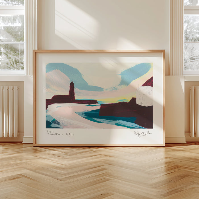 A framed abstract landscape art print leaning against a wall in a bright room with wood floors and large windows.