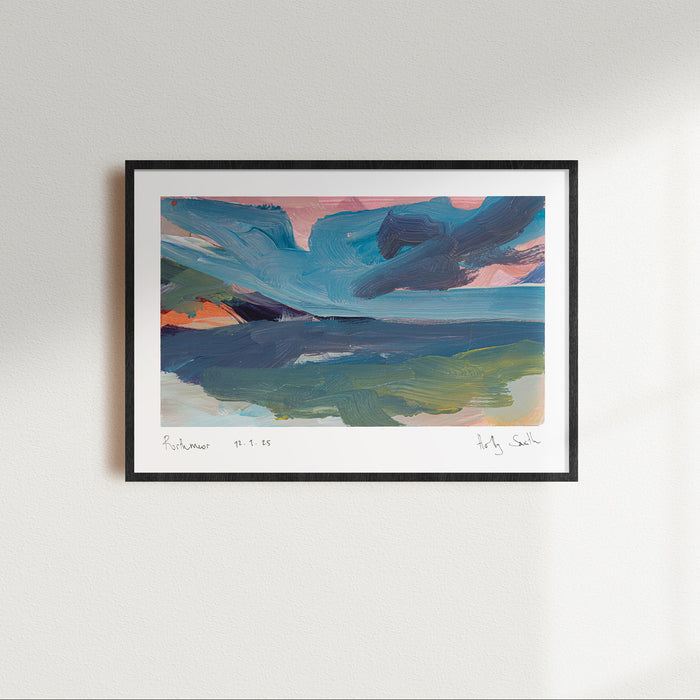 A framed abstract landscape art print featuring blue, green, pink, and orange tones, displayed on a clean white wall with soft window light casting shadows.