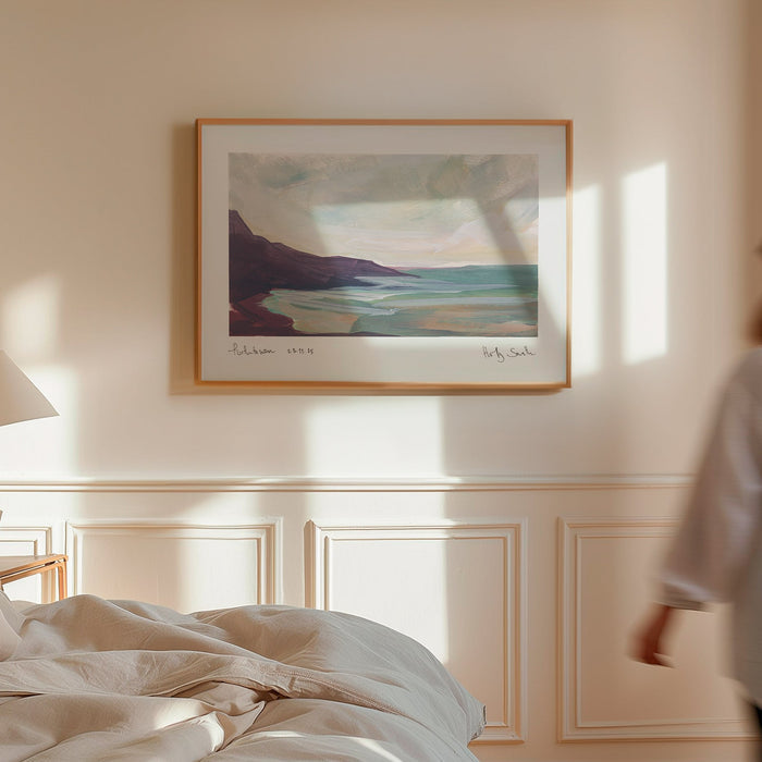A framed landscape art print of Porthtowan in Cornwall in a modern bedroom. Featuring an impressionistic painting of a coastal scene with dark cliffs, turquoise water, and a cloudy sky, shown against a plain white background.