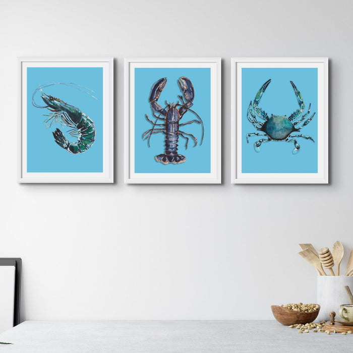 A set of three kitchen art prints of a prawn, crab and lobster in a modern kitchen.