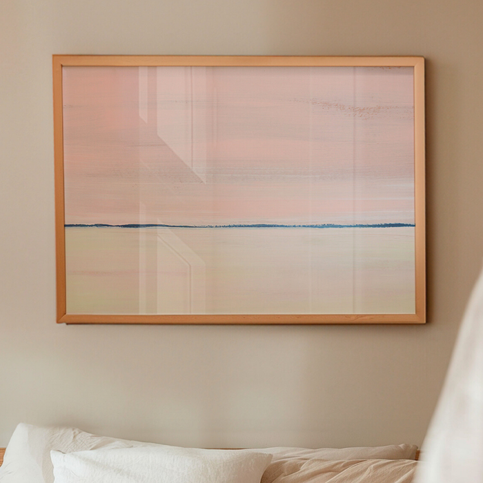 Pink seascape painting with soft horizon line, framed coastal wall art above bed with natural wood frame.