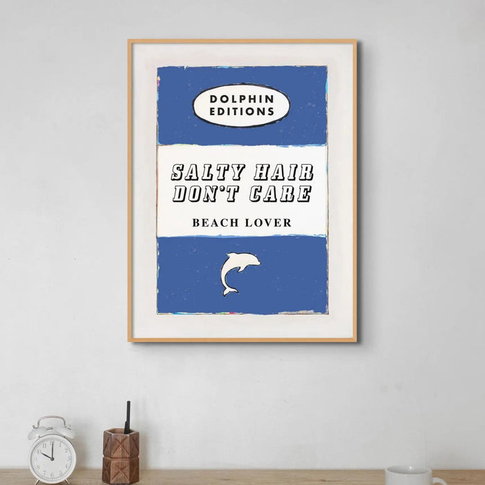 A vintage style book cover art print with the title 'SALTY HAIR DON'T CARE BEACH LOVER' and a small graphic of a dolphin. The background is blue with white and darker blue stripes.
