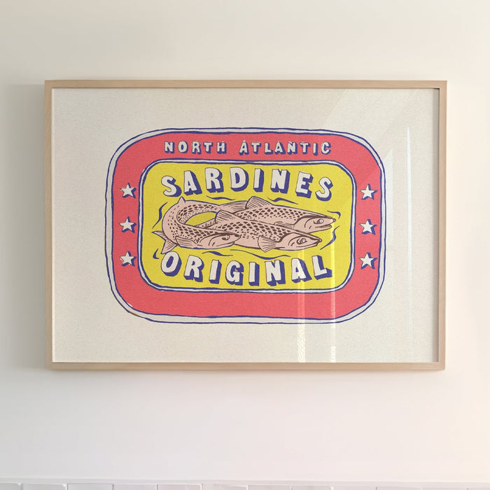 Framed artwork of a vintage sardine tin label with red and yellow colors featuring an illustration of a fish and the text 'SARDINES ORIGINAL'.