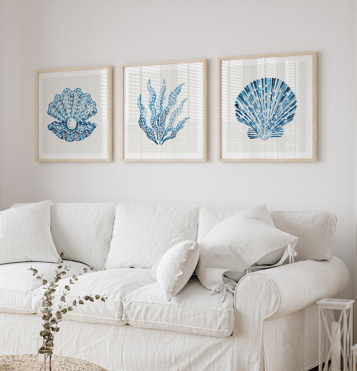 Set of three marine life coastal art pints. White sofa with decorative pillows against a wall with framed blue and white artwork.