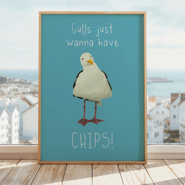 Seagull art print featuring a painted seagull on a blue background with the quote “Gulls just wanna have chips”, framed in a natural wood frame.