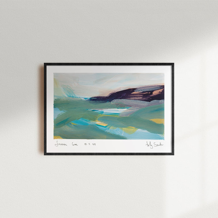A framed abstract landscape painting of Sennen Cove in Cornwall, featuring teal, green, blue, and dark purple brushstrokes on a white mat with a black frame. A framed abstract landscape art print with a black frame and white mat, hanging on a light grey wall with soft window shadows.