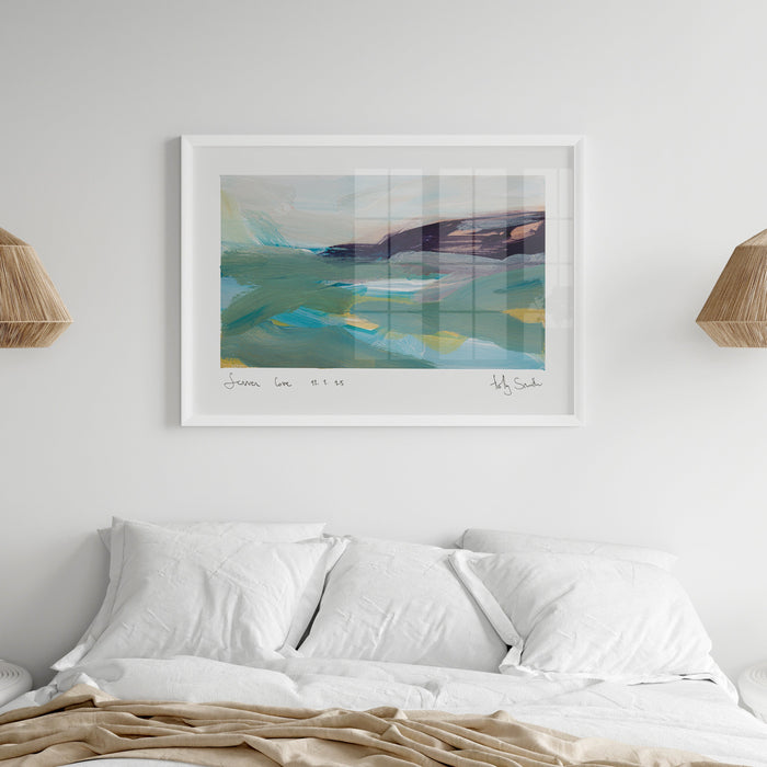 A framed abstract landscape art print hangs on a white wall above a neatly made bed with white pillows and beige bedding. The print features soft blue, green, and purple tones, and is flanked by two woven pendant lights.