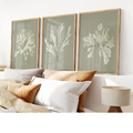 A set of three framed seaweed prints displayed on a wall above a couch, with a neutral color frame and green and olive seaweed illustrations.
