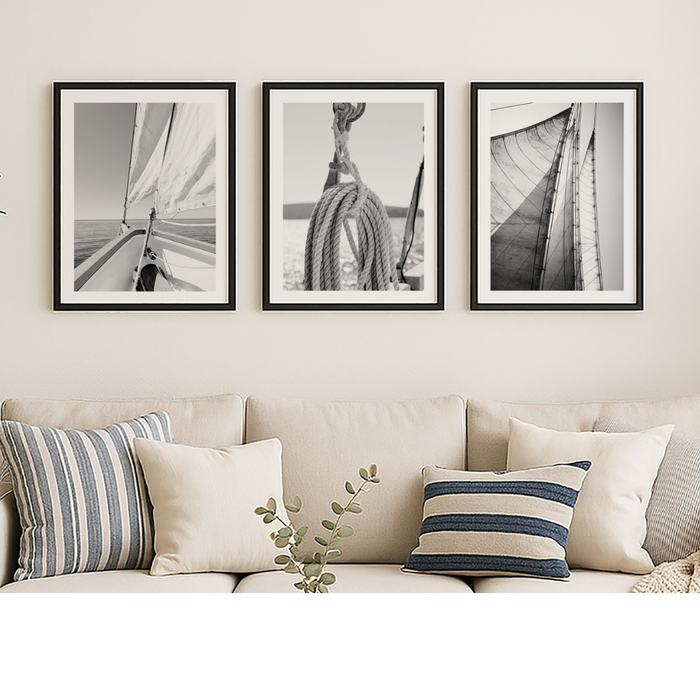 Set of three sailing prints in living room. Three framed black and white sailing photography artworks above a beige sofa with striped cushions.