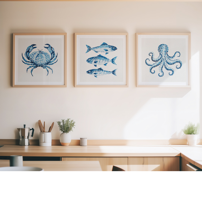 Three framed blue ocean-themed prints featuring a crab, fish, and octopus, displayed on a beige wall above a wooden counter in a modern kitchen setting.
