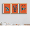 A set of three framed prints featuring colorful illustrations of shellfish on a red background, displayed on a wall.