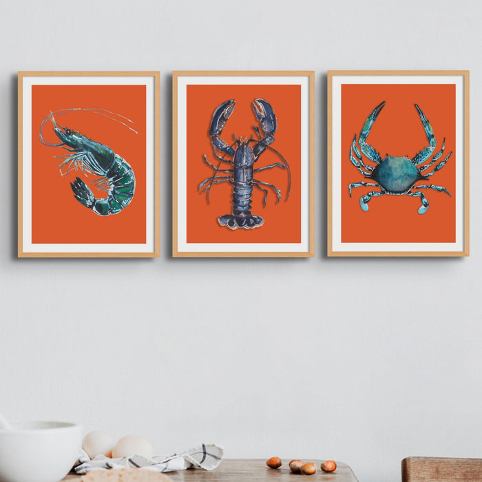 Set of 3 kitchen art print - framed artworks of a blue lobster, crab and prawn on an orange background in dining room.