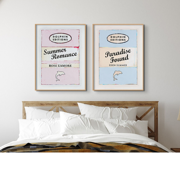 Set of two framed vintage book cover style art prints with quotes, 'Summer Romance' and 'Paradise Found', displayed above a bed.