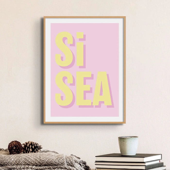 A framed word art print with the text 'Si Sea' in yellow letters on a pink background