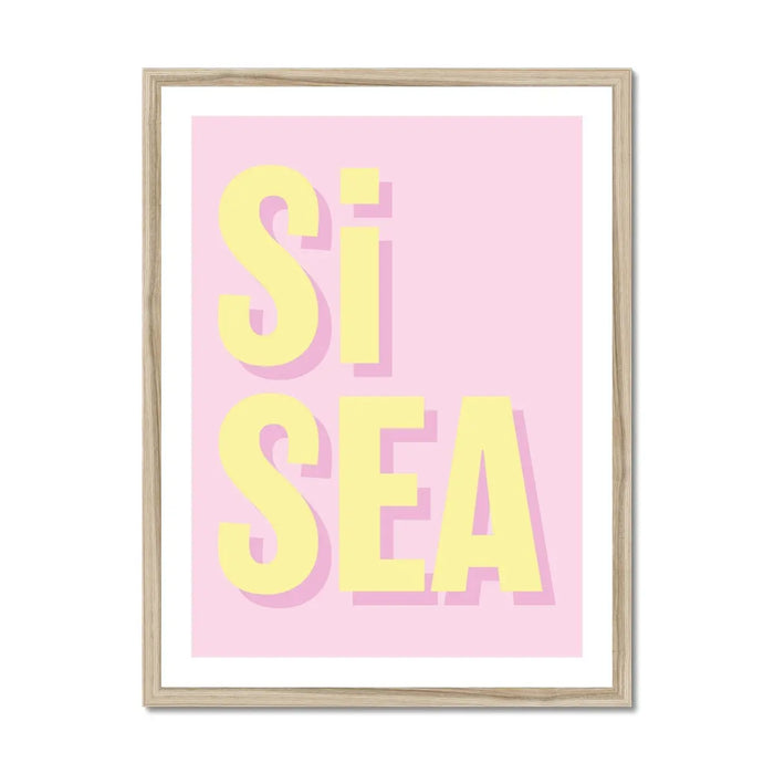 A framed word art print with the text 'Si Sea' in yellow letters on a pink background, encased in a simple wooden frame.