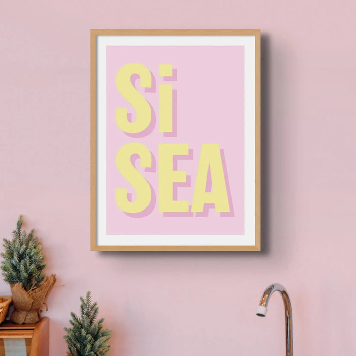 A framed coastal word print with the text 'Si Sea' in yellow letters on a pink background