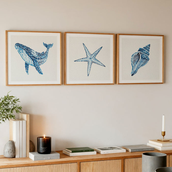 A set of three shel and whale paintings in living room on wall above sideboard.