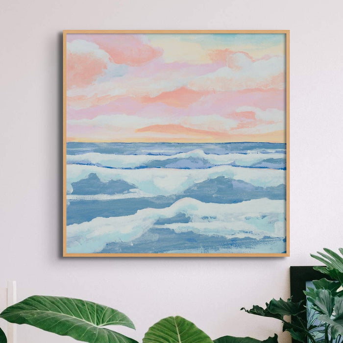 Pink and blue seascape painting with soft sunrise sky over ocean waves, coastal wall art print in living room with plants