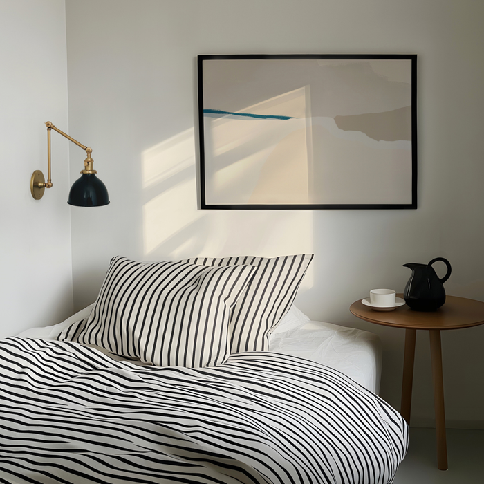 Modern bedroom with striped bedding, wall lamp, and abstract art.