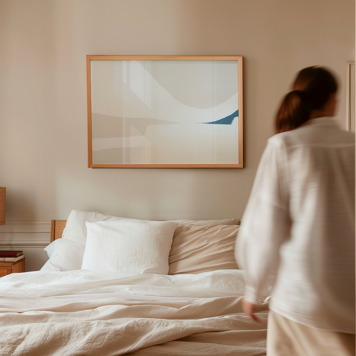 Person standing by a bed in a bedroom with abstract art on the wall.