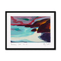 A framed abstract landscape painting featuring turquoise water, dark red and purple rocks, and pink sky, presented in a black frame with a white mat and handwritten signature at the bottom.