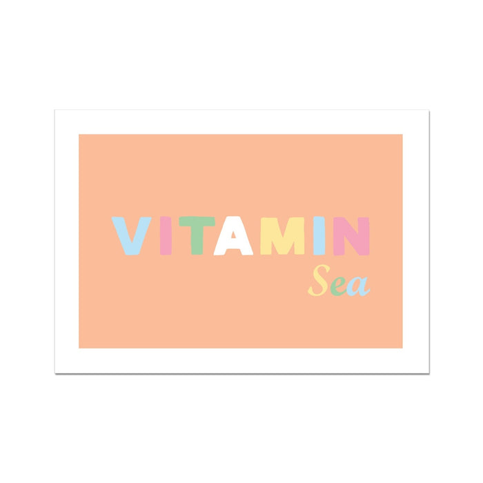An art print with the text 'VITAMIN Sea' on a peach-colored background, presented in a simple white frame.