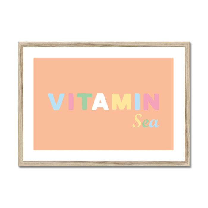 Framed art print with the text 'VITAMIN Sea' on a peach background, displayed in a light wood frame.