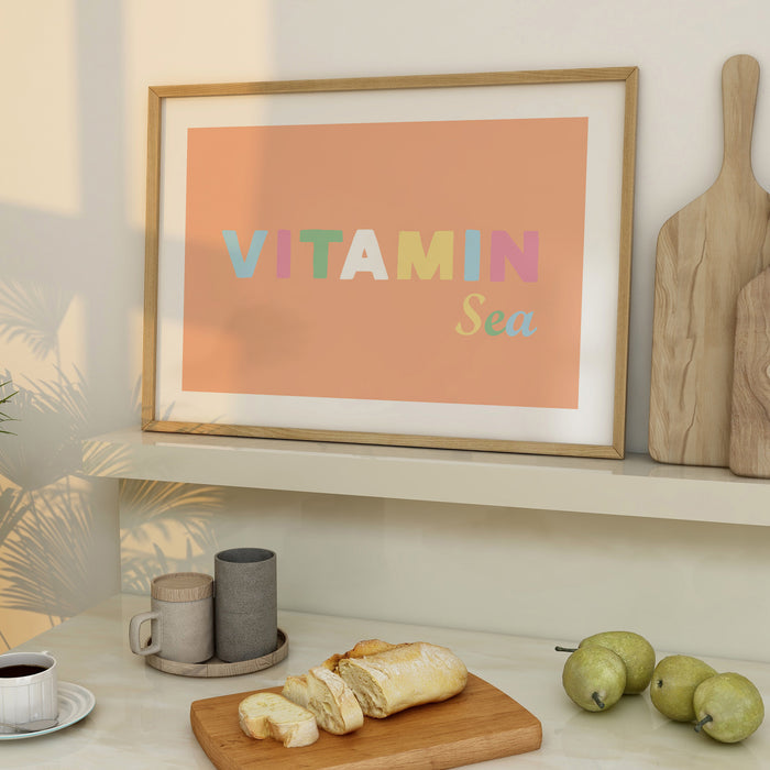 Framed art print in kitchen with the text 'VITAMIN Sea' on a peach background, displayed in a light wood frame.