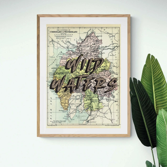 Framed Lake District vintage map art print with the text 'WILD WATERS' overlaid on a map background, in a light wood frame.